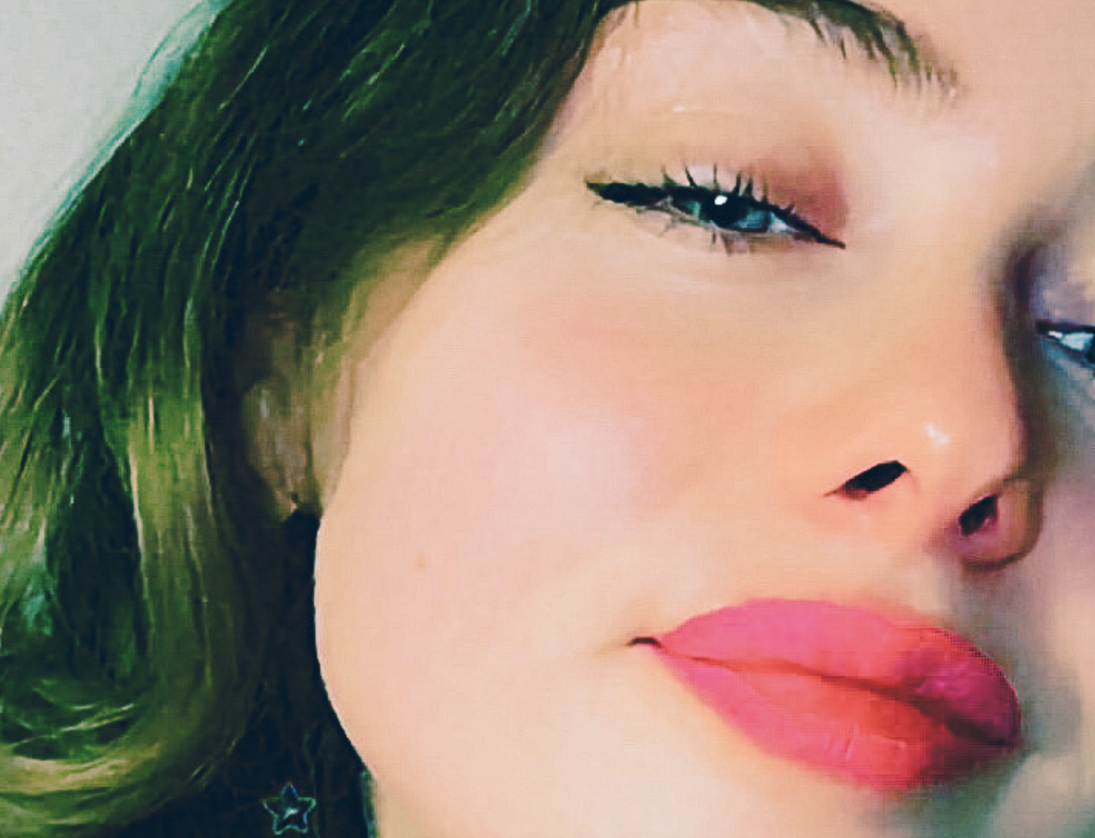 Close-up of a woman's face featuring bright pink lips and a slight smile, with her greenish hair framing the side of her face.